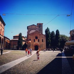People walking on road amidst buildings against clear blue sky