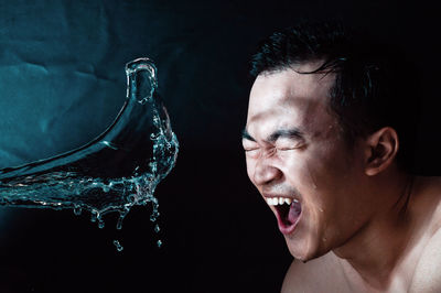 Close-up of shirtless man making face by water against black background