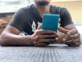 Midsection of man holding cigarette while using mobile phone 