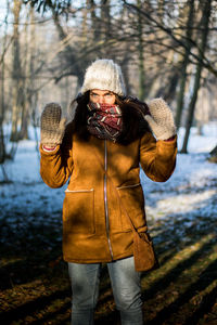 Portrait of woman with arms raised standing in forest during winter