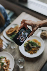 Hand with cell phone photographing food on table