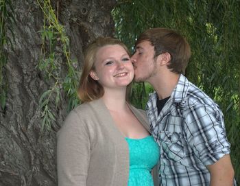 Man kissing on cheek of girlfriend against tree