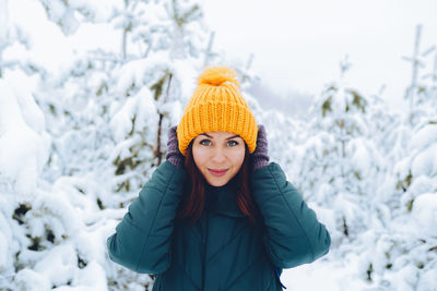 Cheerful girl with red hair in warm clothes playing with snow outdoors near the beautiful forest