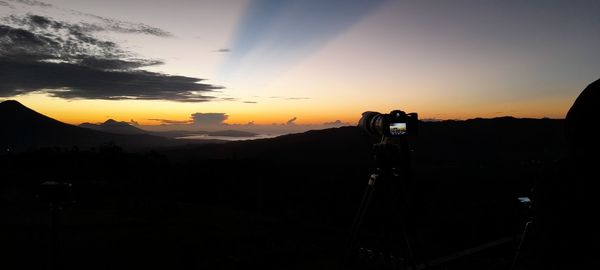 Silhouette of camera against sky during sunset