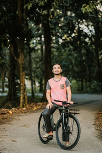 Portrait of young man riding bicycle on street against forest