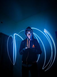 Young man standing against illuminated light painting