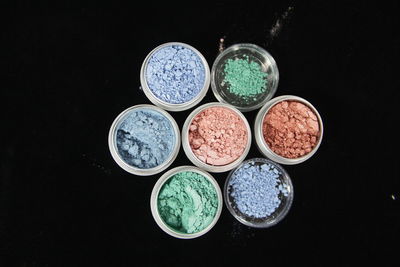 Directly above shot of multi colored face powder in containers against black background