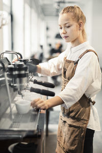 Young female barista using coffee maker at cafe