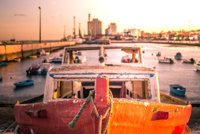 Close-up of boats moored at harbor against sky during sunset