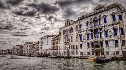 View of canal and buildings against cloudy sky