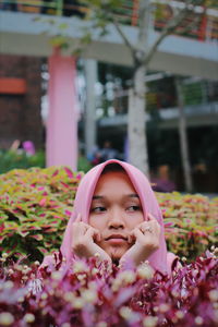 Thoughtful teenage girl wearing hijab amidst flowers in city
