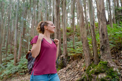 Woman standing by tree trunk in forest