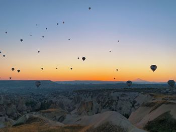 Hot air balloons flying over silhouette landscape against sky during sunset