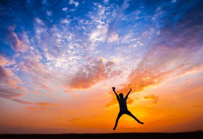 Silhouette woman with arms raised against sky during sunset