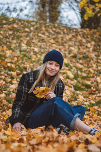 Smiling and happy brunette sitting in a pile of colourful leaves in a city park