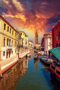 Canal amidst buildings against sky during sunset