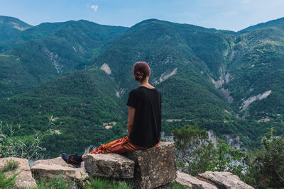 Rear view of man sitting on rock looking at mountains