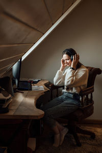 Young woman listening to music in big headphones near computer at home. creating play list, enjoying