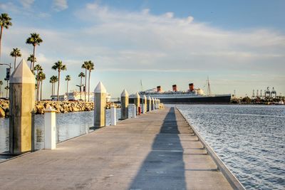 Narrow walkway leading to calm sea against sky