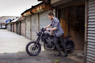 Man pushing motorcycle outside workshop