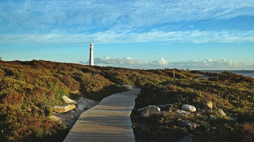 Boardwalk leading towards sea against cloudy sky