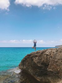 Woman standing on rocky shore against blue sky