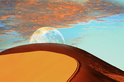 Dune 45 in the namib naukluft at dusk with the moon peeping over the top of the bright orange peak