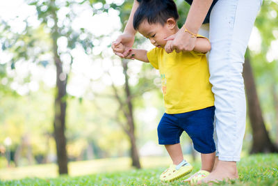 Low section of mother assisting baby son in walking on grassy land