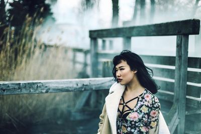 Young woman standing by railing against water