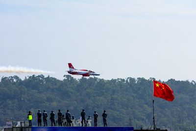 Army soldiers looking at fighter plane flying in sky