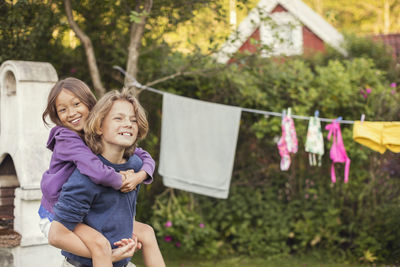 Happy teenage boy giving piggyback ride to friend at back yard