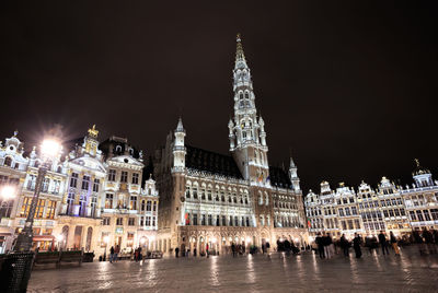 People on town square against illuminated buildings at night