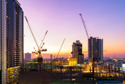 Cranes at construction site against sky during sunset