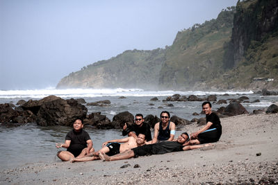 People sitting on beach by sea against sky