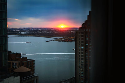 Illuminated buildings by sea against sky during sunset