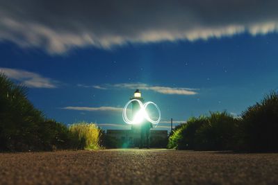 Man performing light painting on pathway leading towards light house against sky