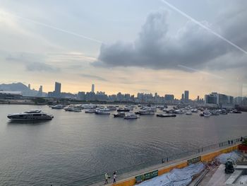 Boats in sea by buildings against sky during sunset