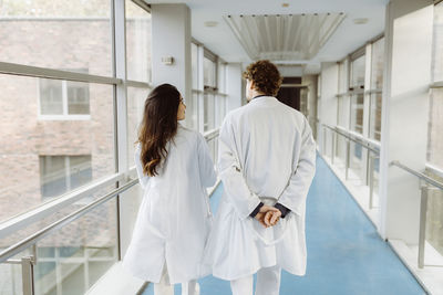 Rear view of male and female doctors discussing while walking together in hospital corridor