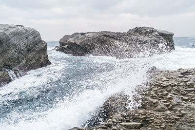 Sea waves splashing on rocks against sky