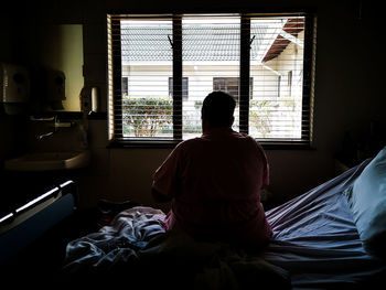 Rear view of man sitting on bed at home