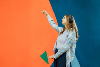 Portrait of woman with arms raised standing against yellow background