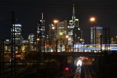 Illuminated street amidst buildings against sky at night