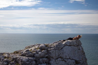 Woman lying on cliff against cloudy sky