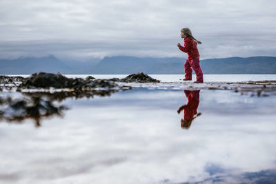 Rear view of woman walking on beach against sky