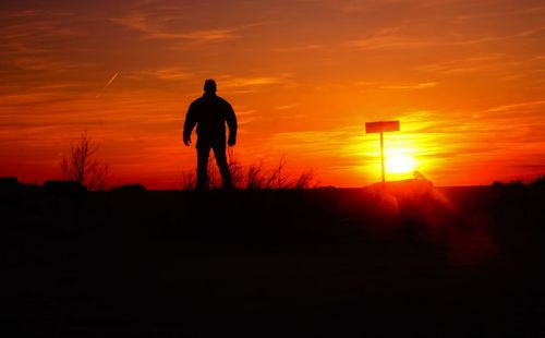 Silhouette man standing on field against orange sky