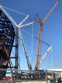 Low angle view of cranes against clear blue sky