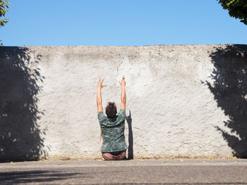 Rear view of man gesturing while sitting against wall