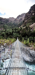 Footbridge amidst trees and mountains against sky