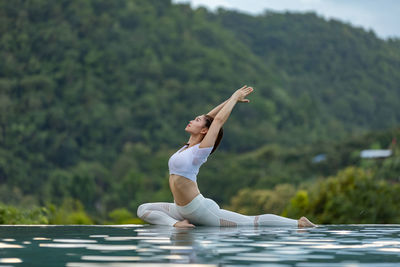 Full length of woman meditating by swimming pool