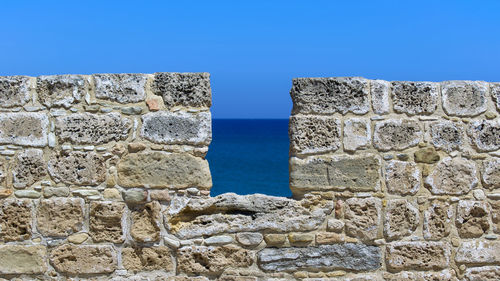 Stone wall by sea against clear blue sky